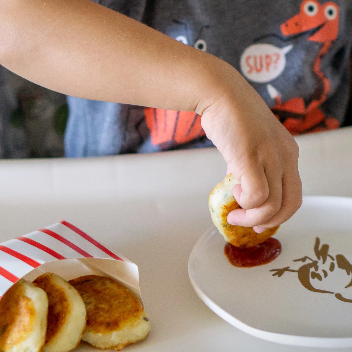 toddler dipping potato nugget in ketchup