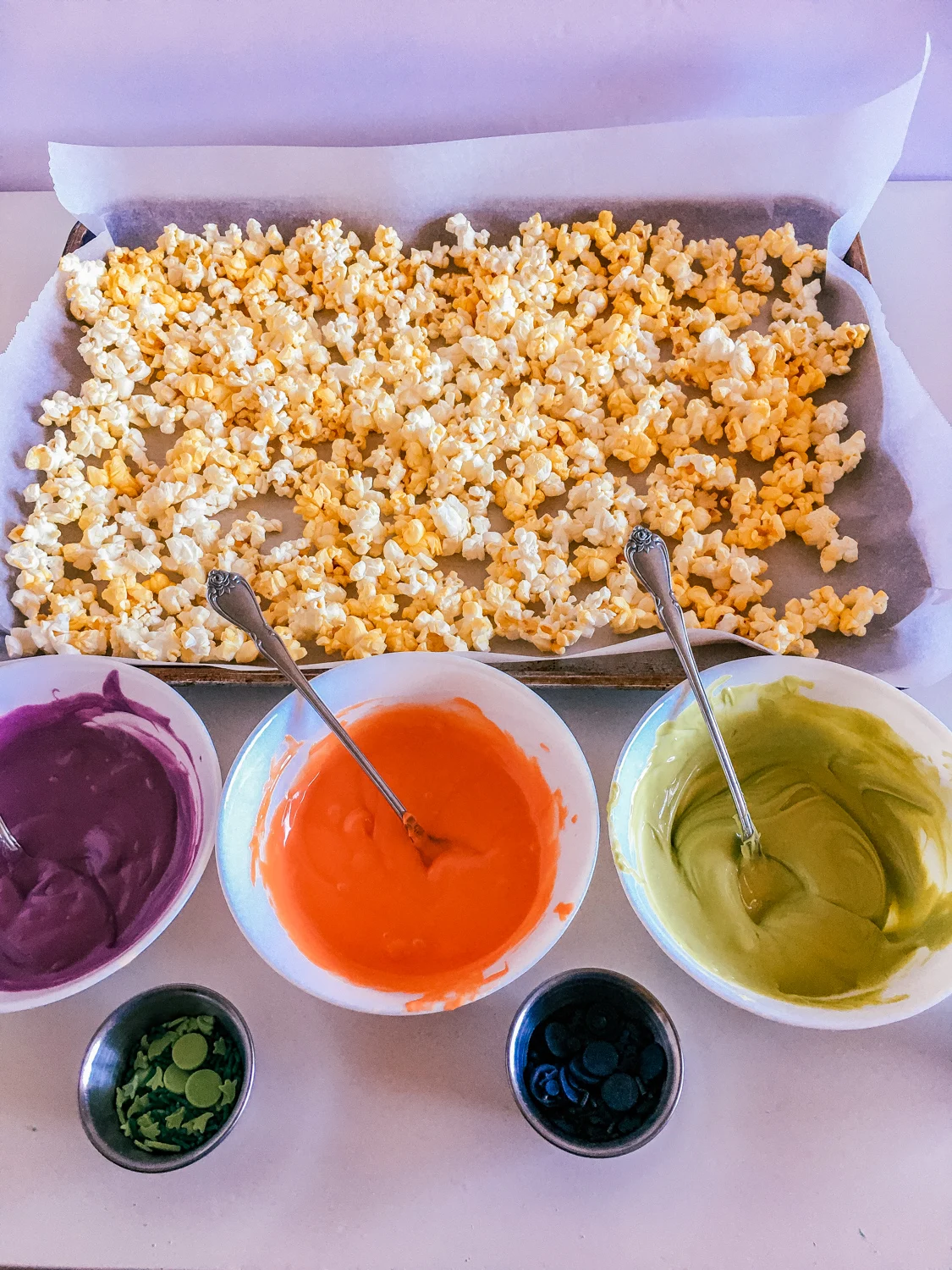 popped popcorn and halloween colored candy melts melted in bowls