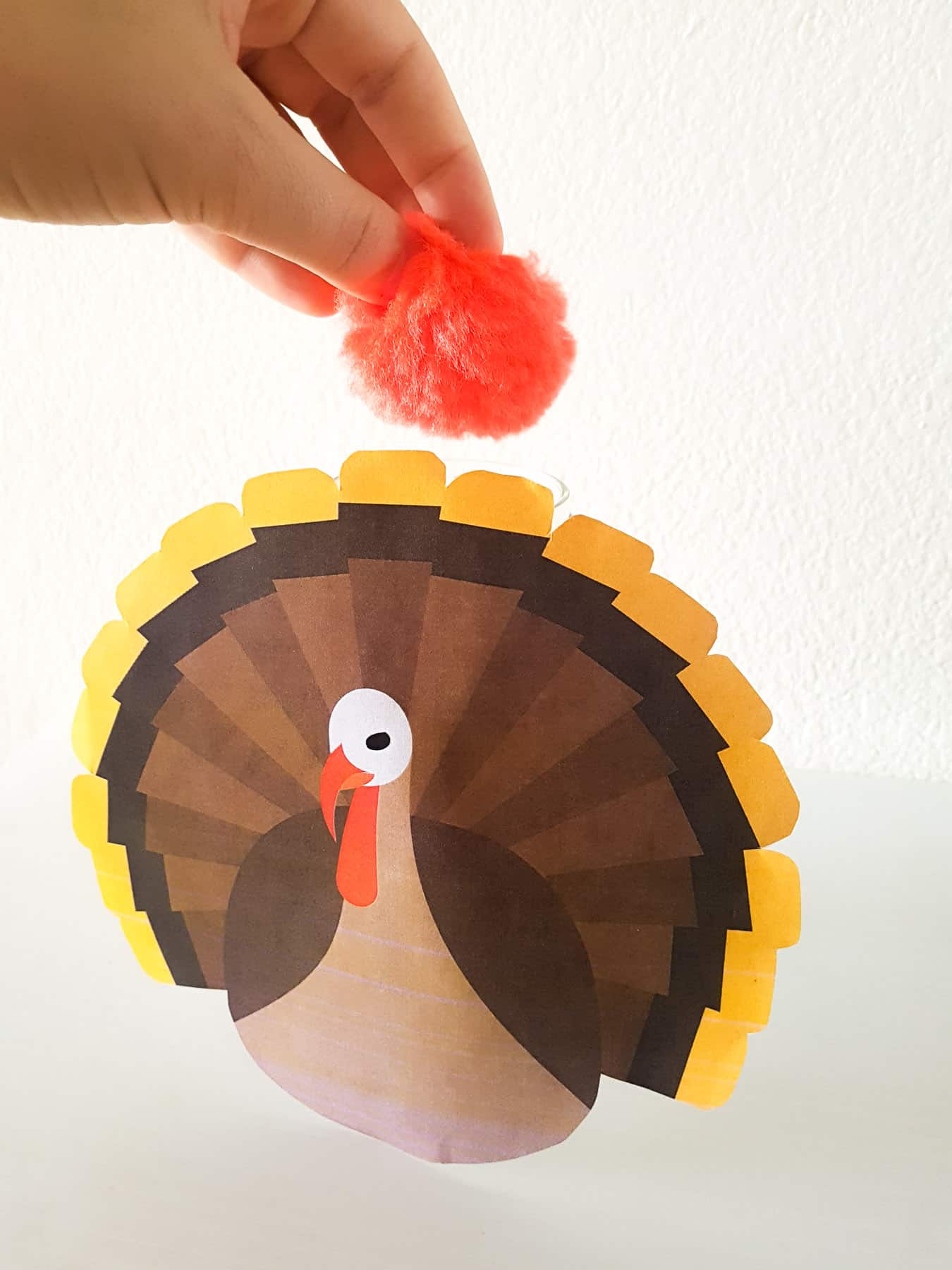 hand putting pompom into a jar with a paper turkey glued to it - demonstrating a toddler activity