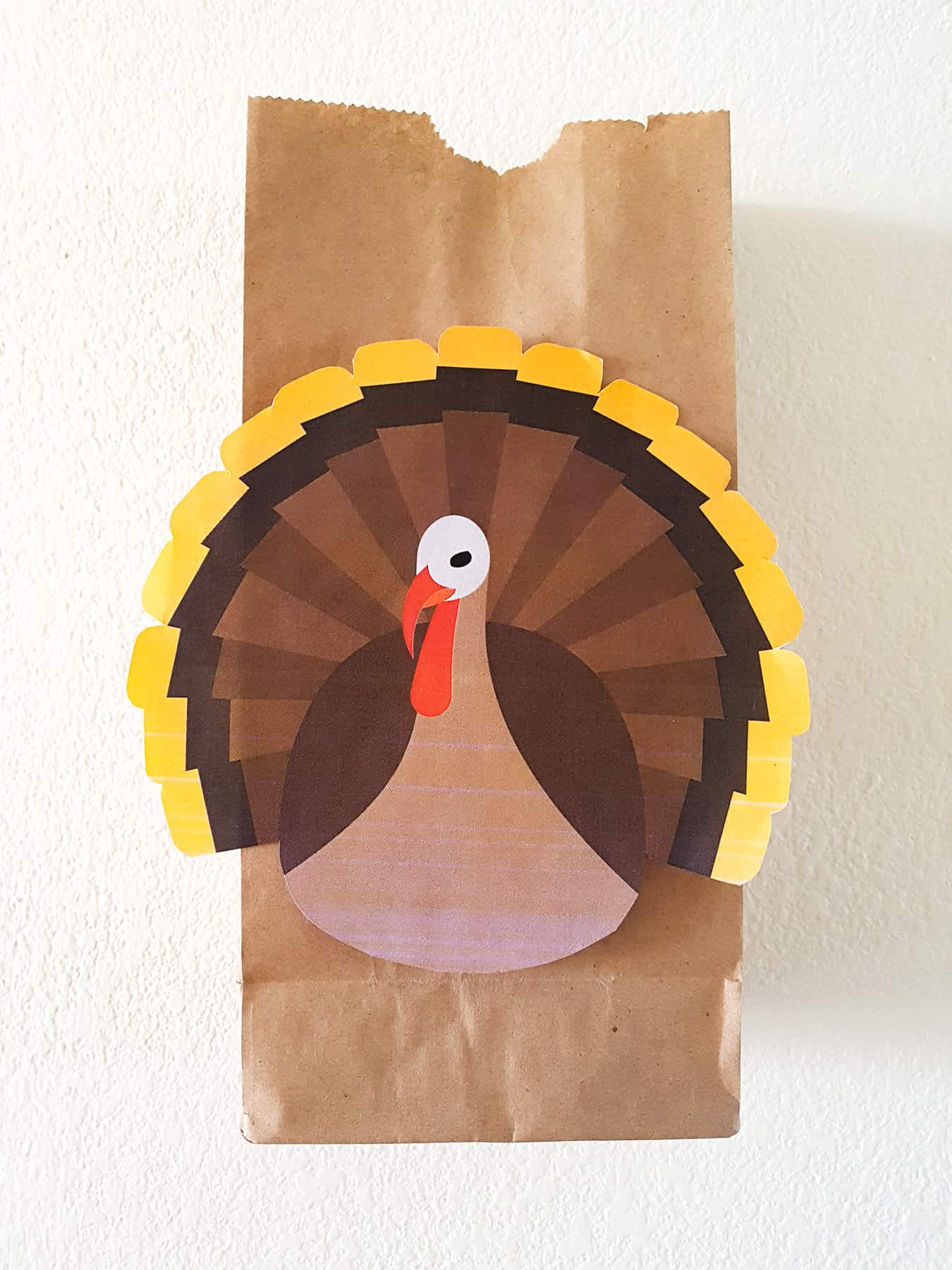 paper bag decorated with a thanksgiving turkey taped to a wall - demonstrating a thanksgiving toddler activity