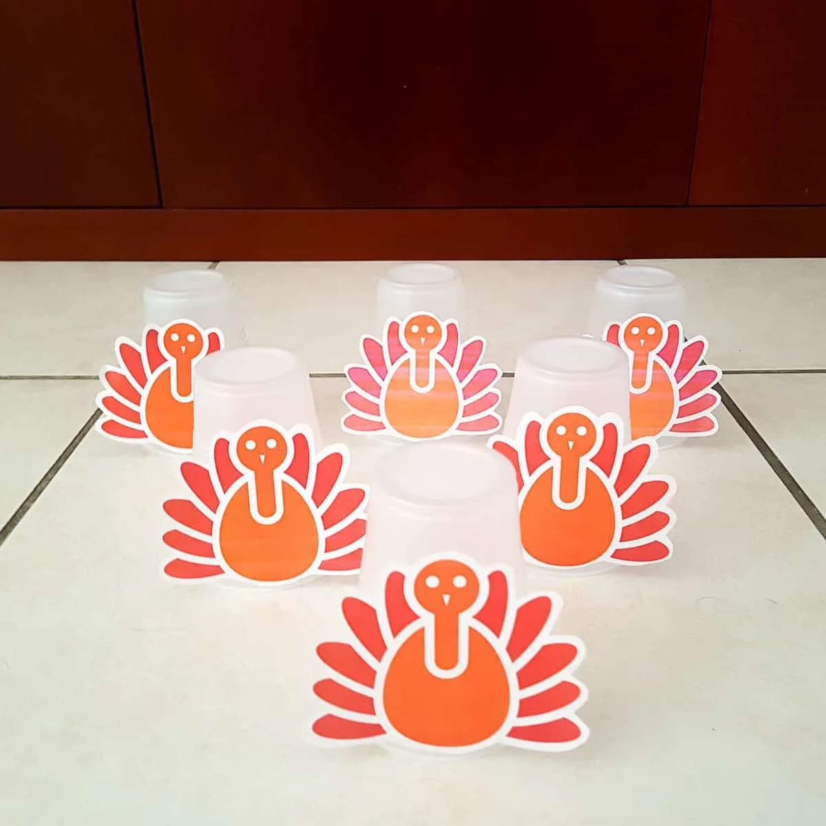 plastic cups with paper thanksgiving turkeys glued to them lined up like bowling pins to demonstrate a toddler thanksgiving bowling activity