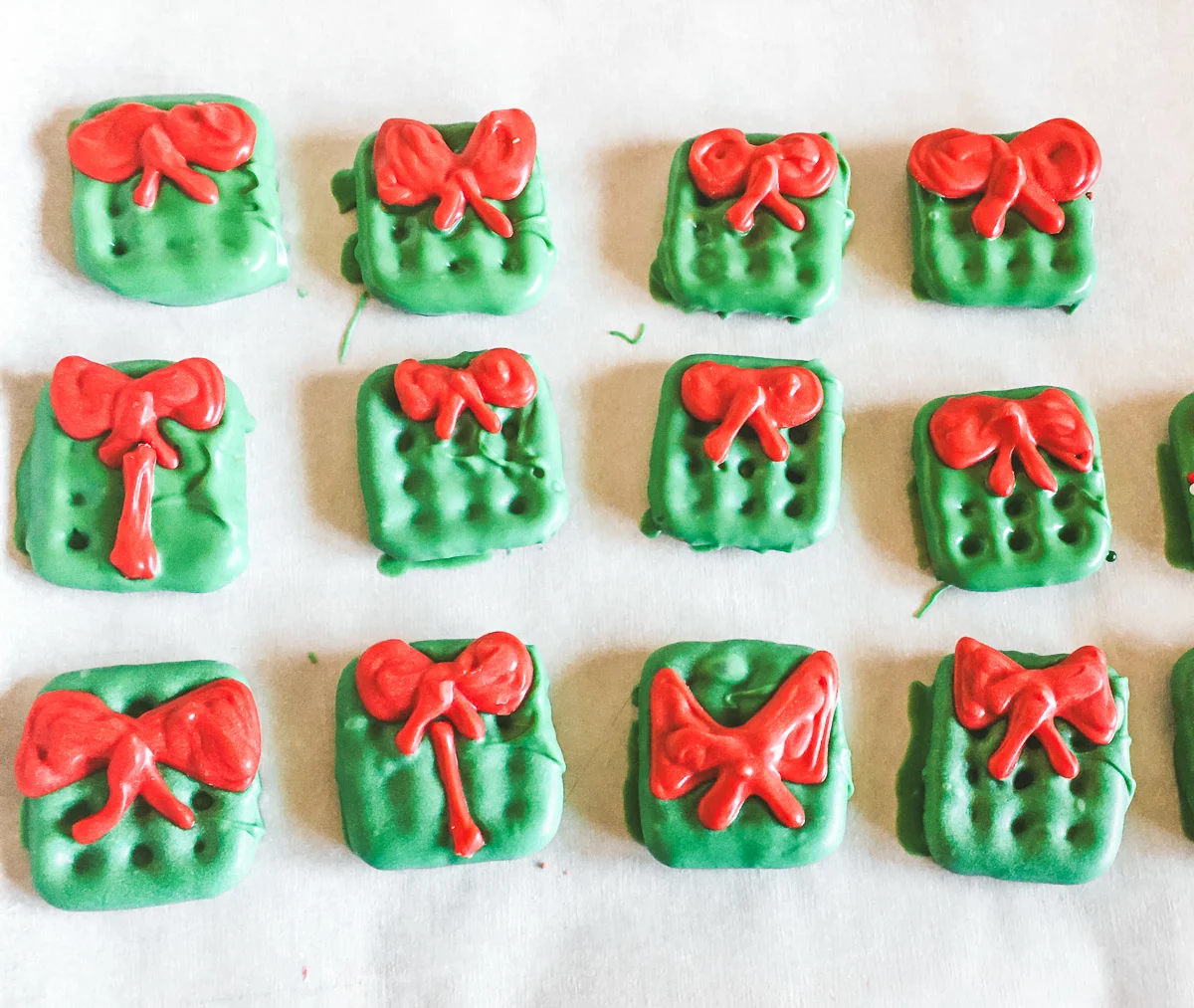 Christmas pretzels decorated like gift boxes with bows laying on parchment paper drying