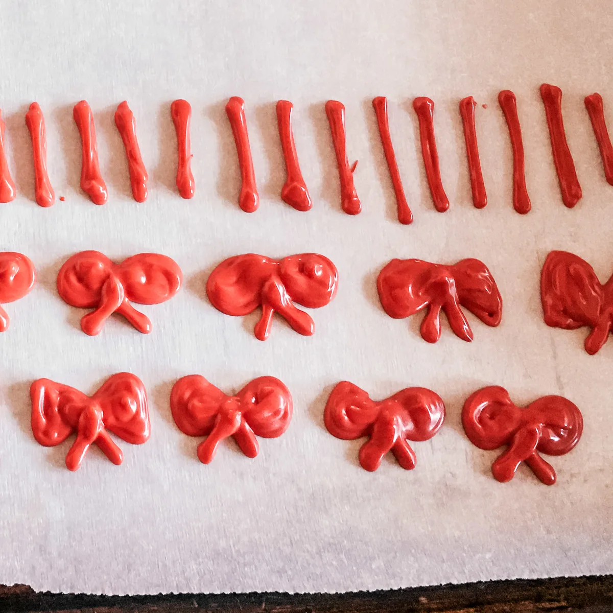 red bows made of melted white chocolate drying on parchment paper
