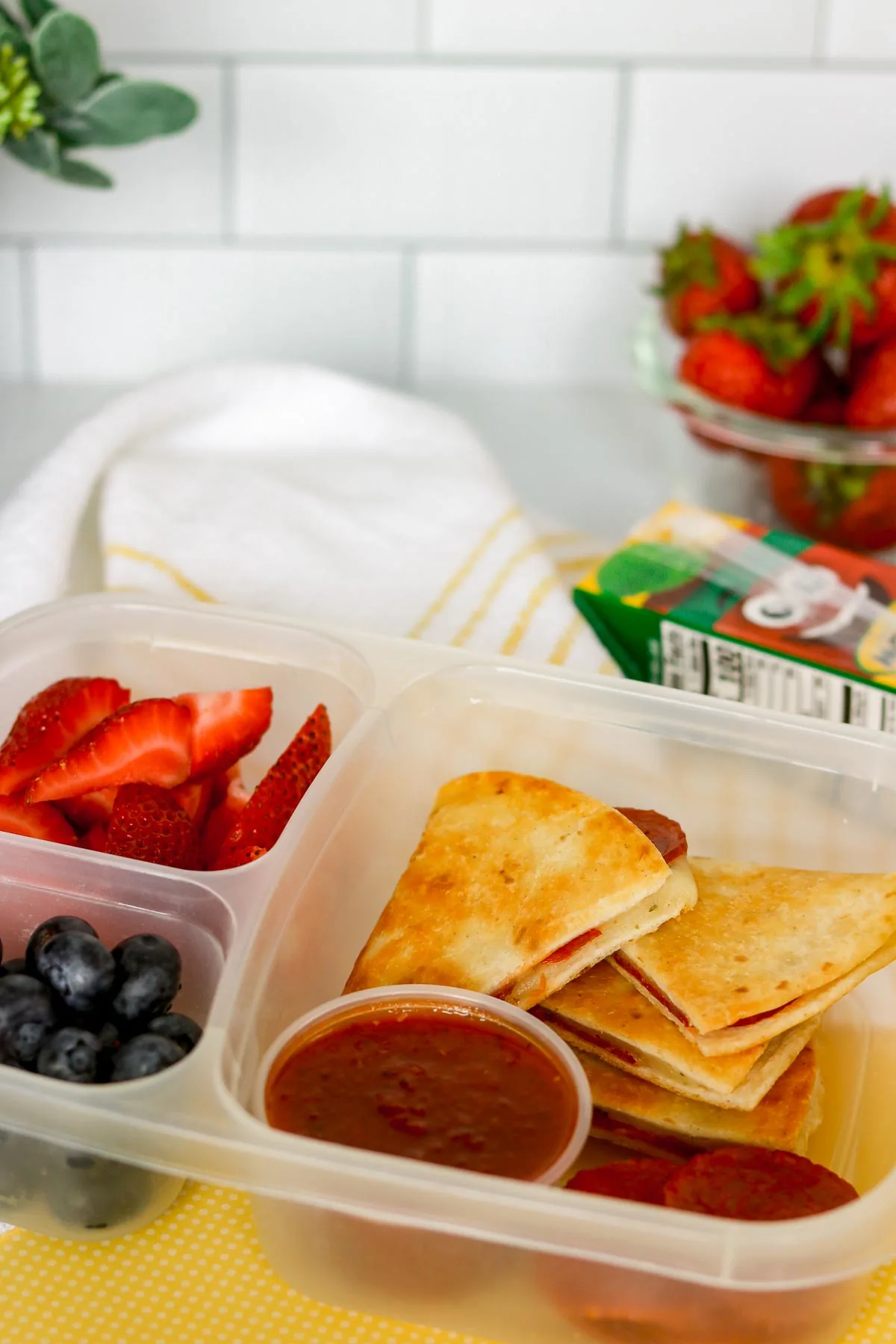 Pepperoni pizzadillas packed for a kid's lunch in a bento box with berries.