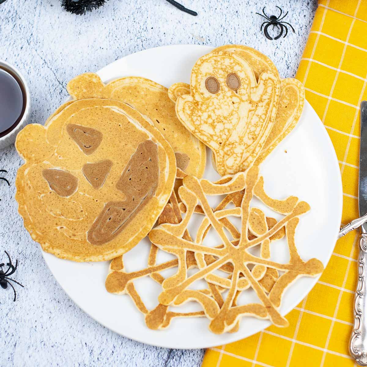 A plate with a spider web pancake, a Jack o lantern pancake, and a ghost pancake for Halloween breakfast.