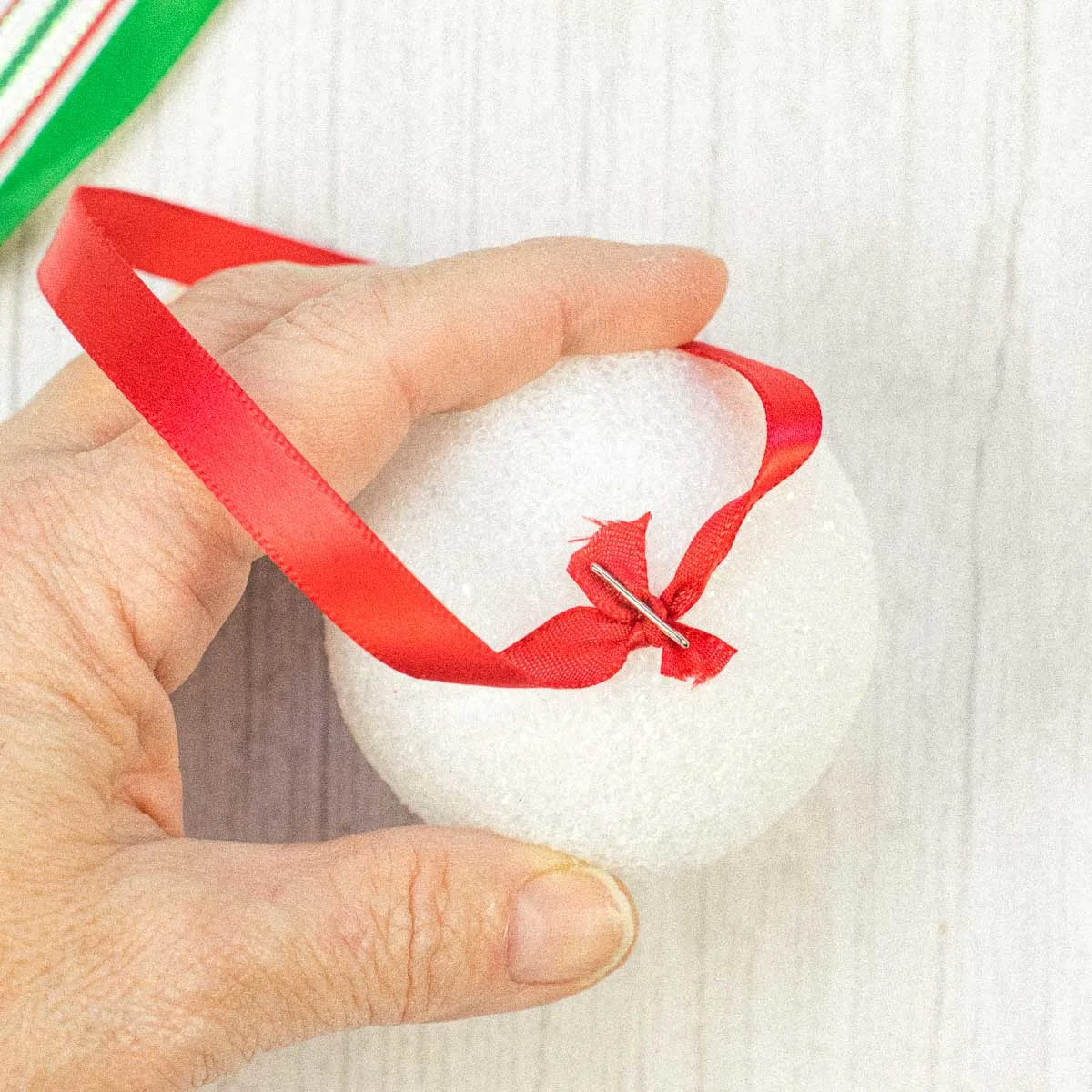 A T pin pierced through a ribbon to attach it to a Styrofoam ball.