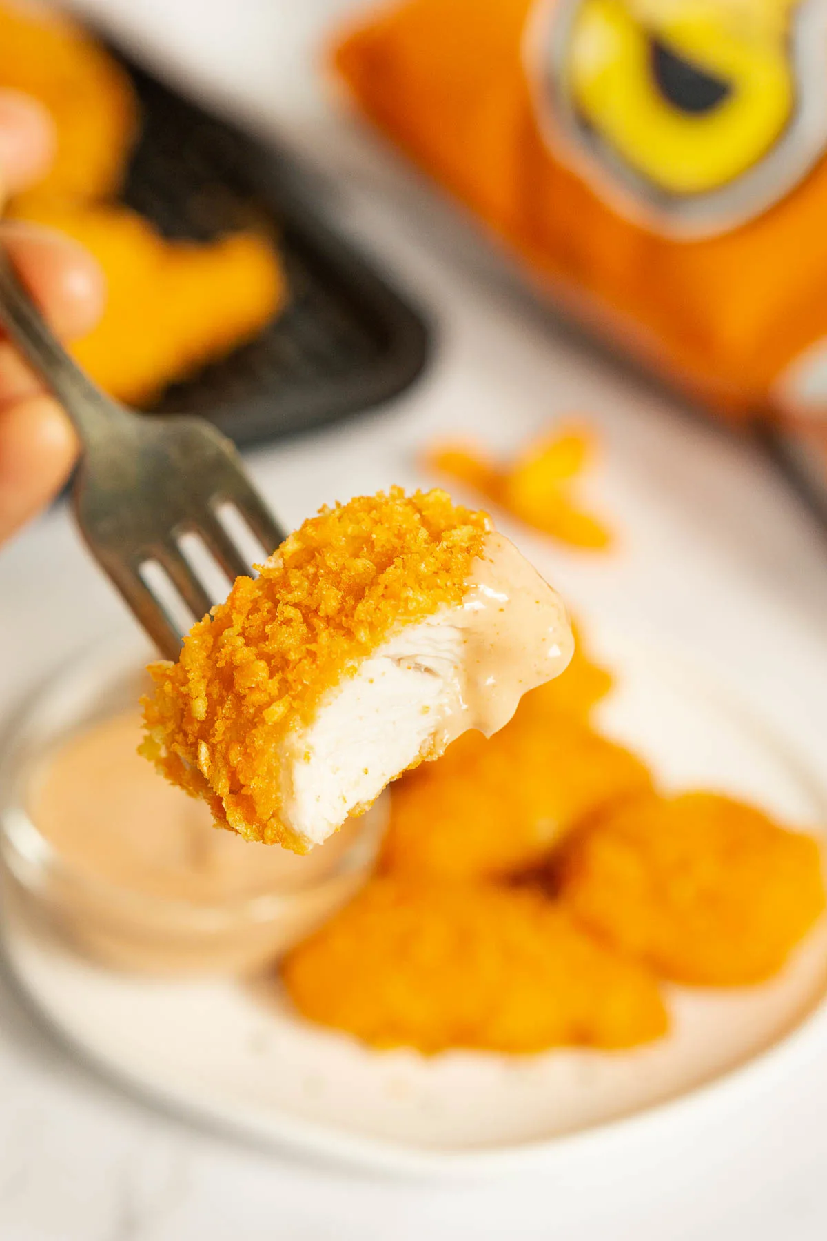 Fork holding Cheetos crusted chicken nugget bit in half to show texture inside. 