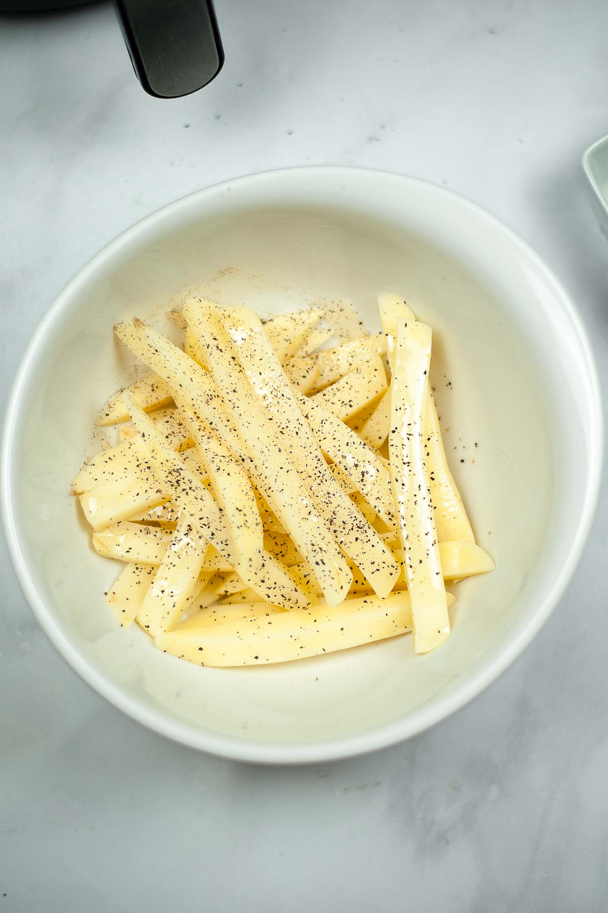 French fry cut potatoes in a bowl with salt and pepper
