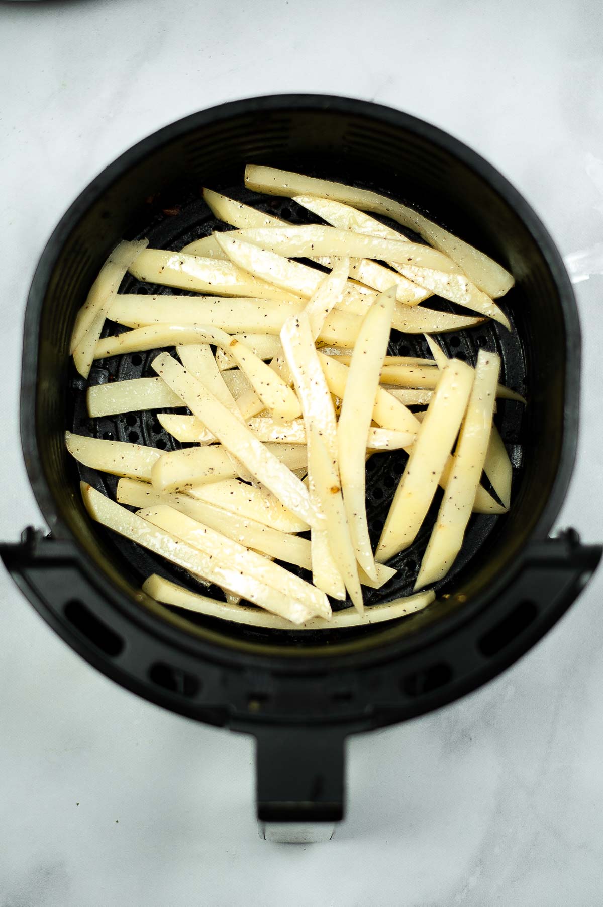 Uncooked potato fries in an air fryer basket