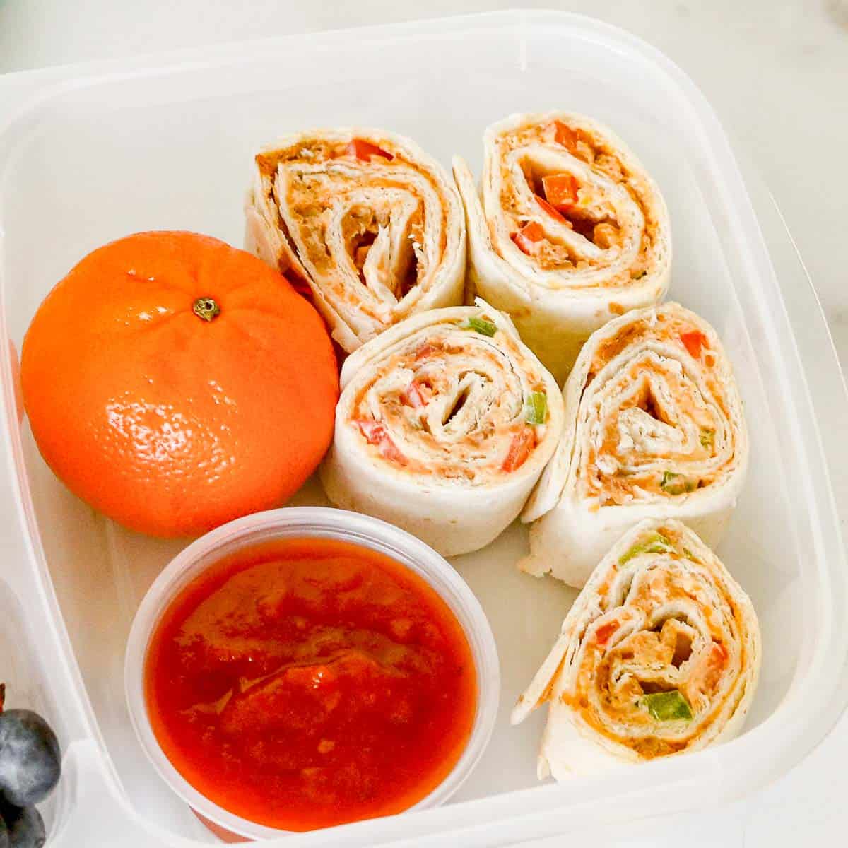 Taco pinwheels with salsa for dipping in a lunch container