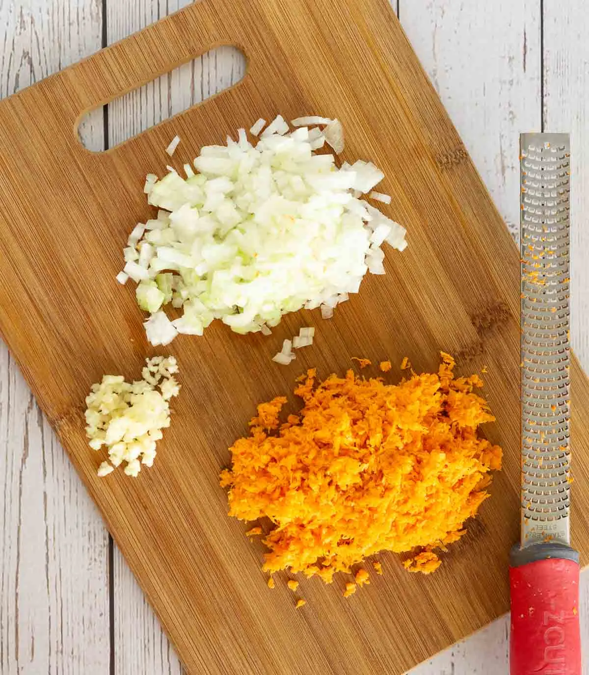 Cutting board with finely grated carrot, diced onion, and minced garlic