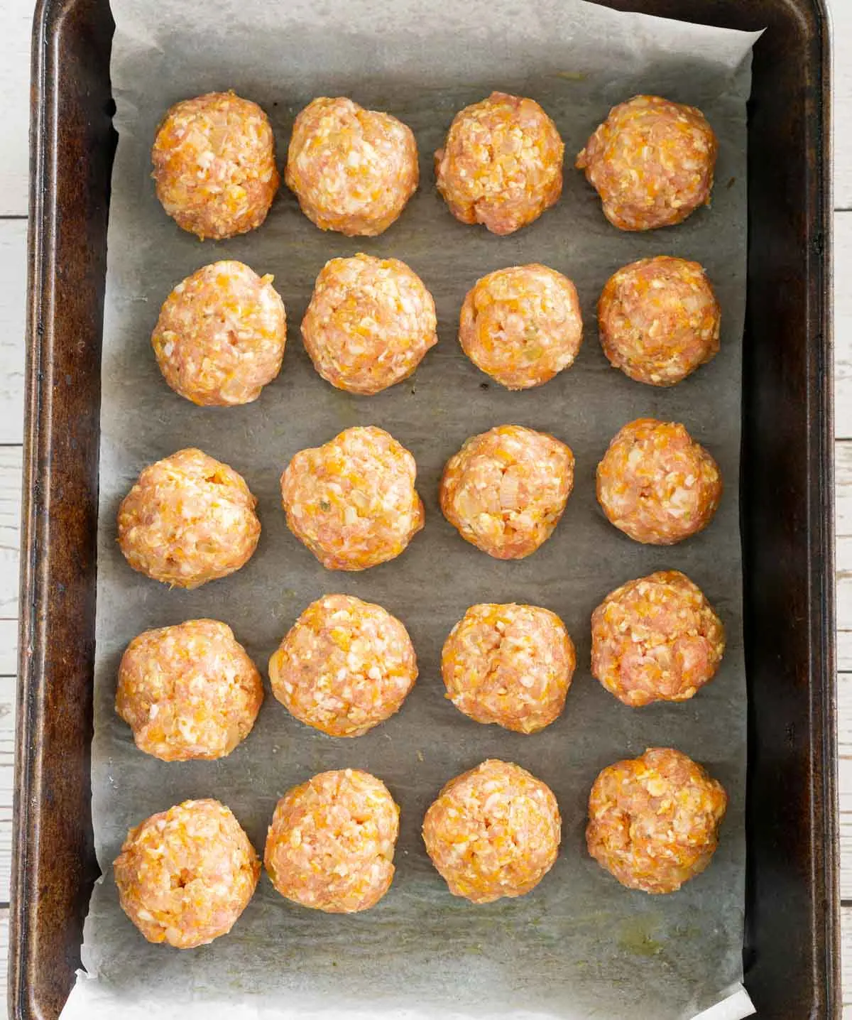 Uncooked pork meatballs arranged on a baking sheet with parchment paper
